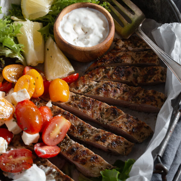 Greek Souvlaki pork tenderloin on platter with tzatziki and tomato salad