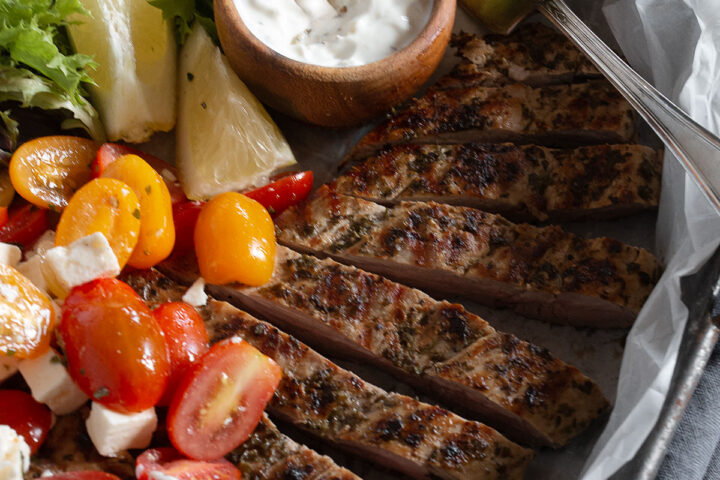 Greek Souvlaki pork tenderloin on platter with tzatziki and tomato salad