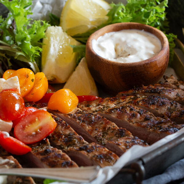 Souvlaki marinated pork tenderloin on a platter with a marinated cherry tomato salad.