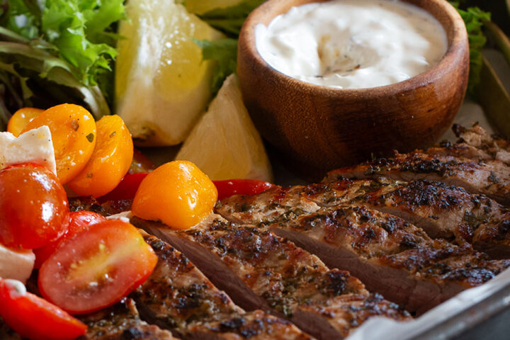 Souvlaki marinated pork tenderloin on a platter with a marinated cherry tomato salad.