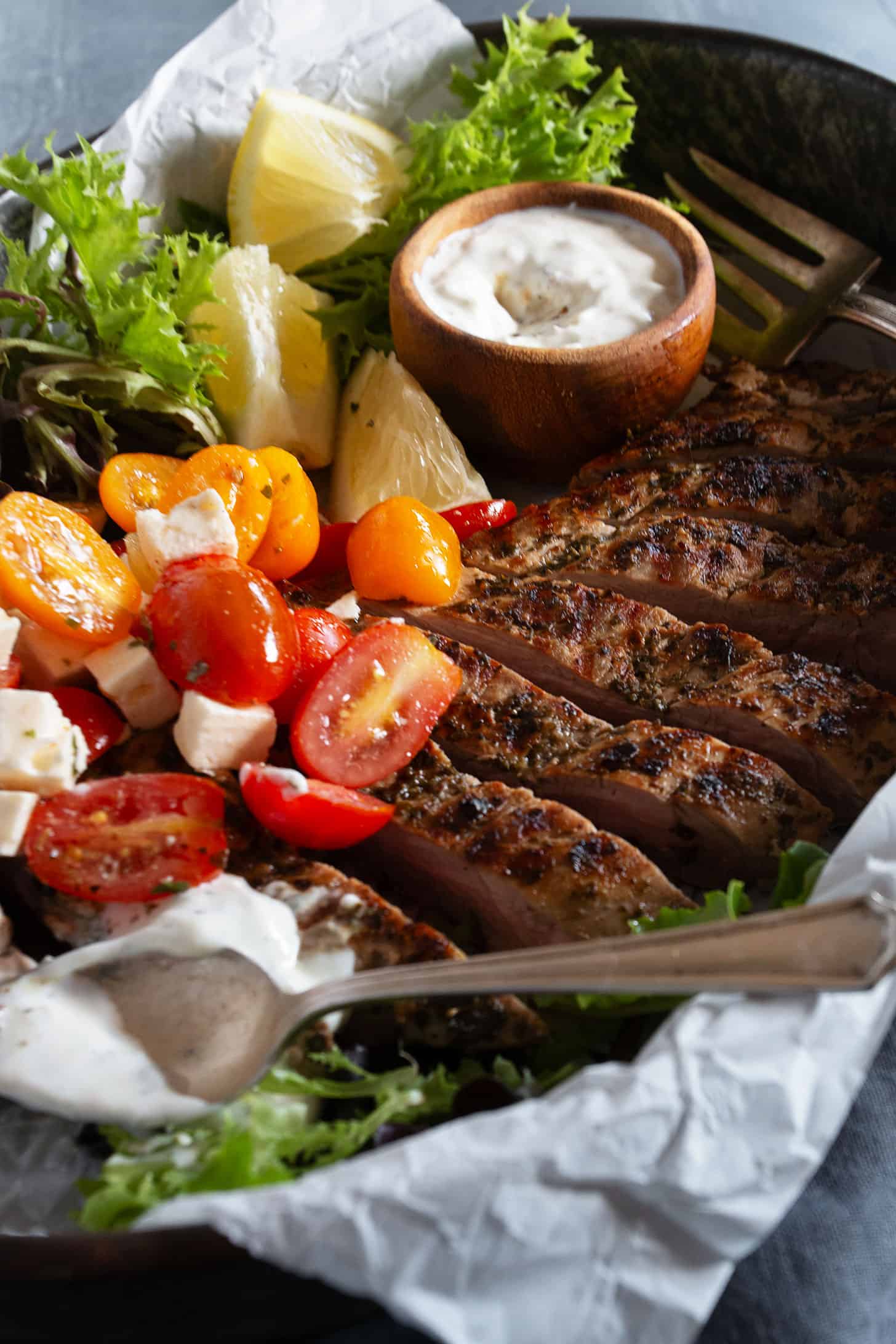 Souvlaki marinated pork tenderloin on a platter with a marinated cherry tomato salad.