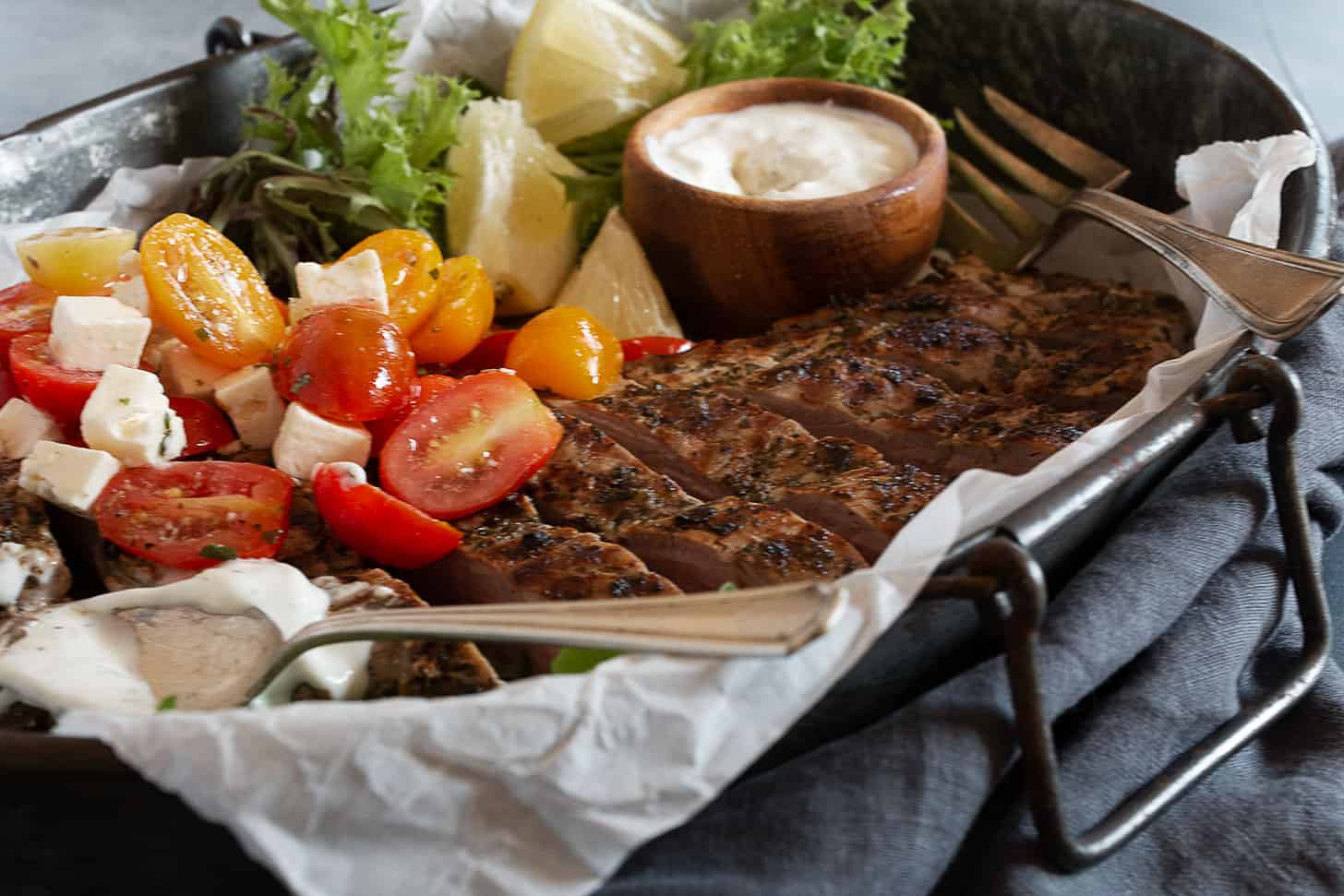 Greek Souvlaki pork tenderloin on platter with tzatziki and tomato salad