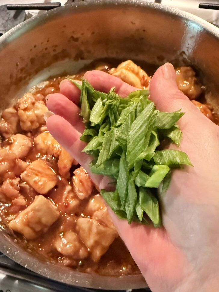 Adding green onion to the skillet.
