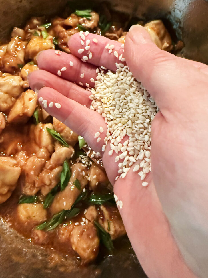 Finishing the spicy chicken with a sprinkling of sesame seeds.