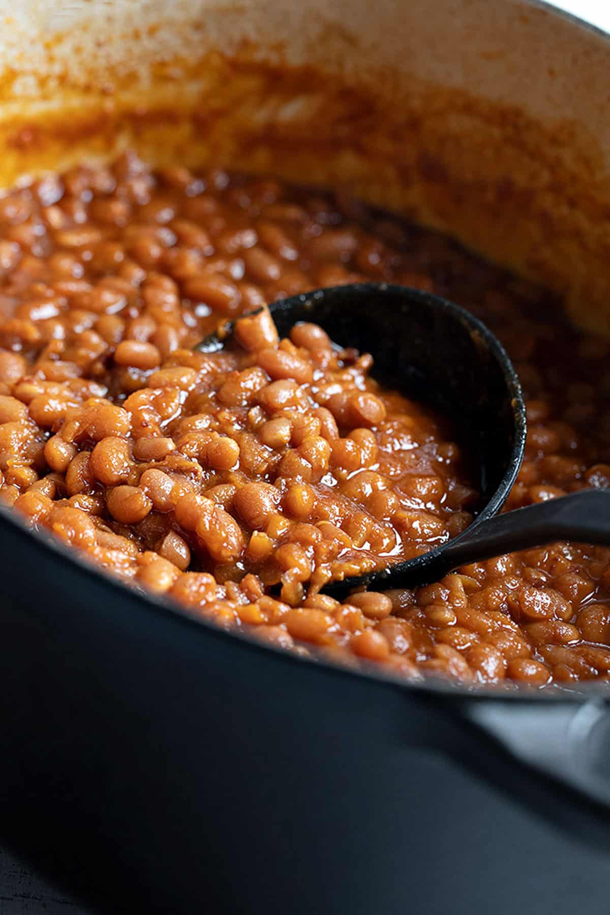 homemade baked beans in black casserole with ladle