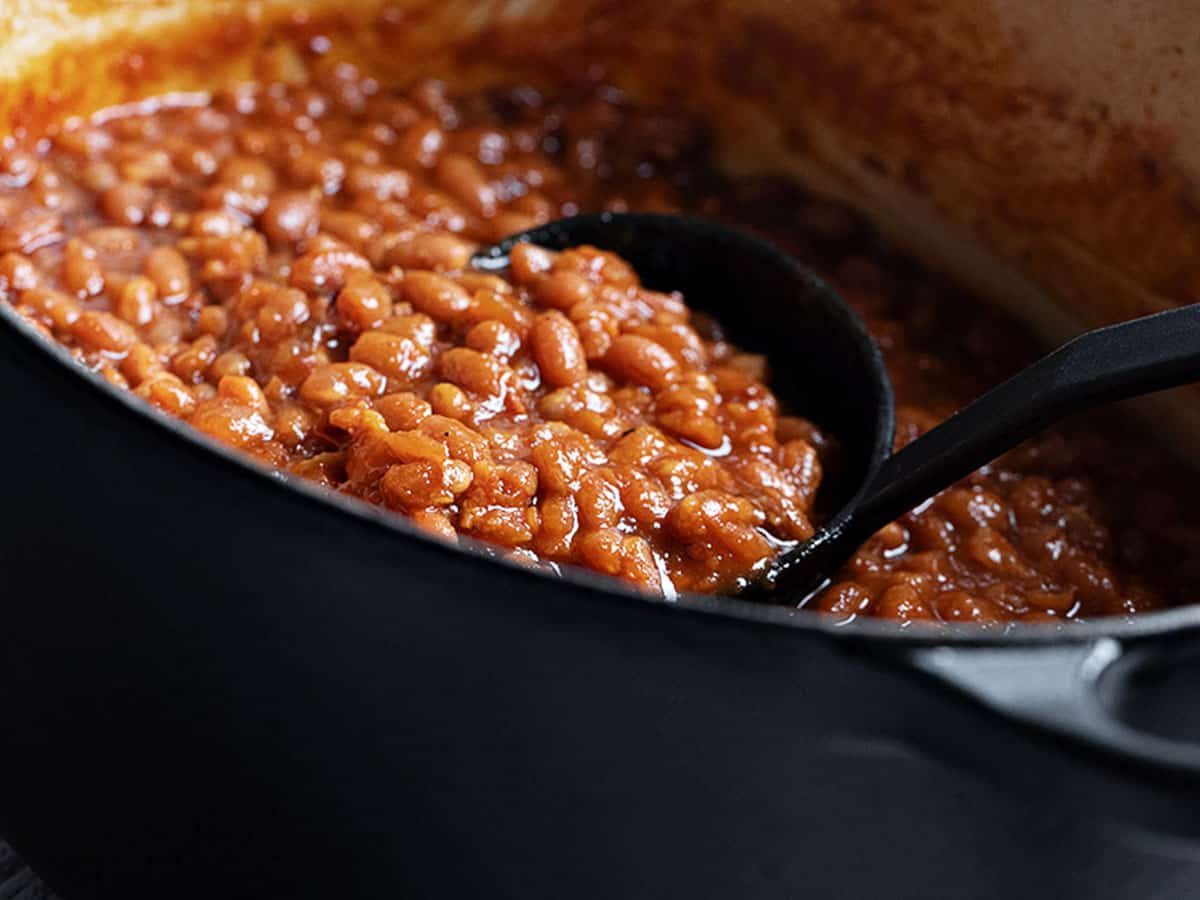 homemade baked beans in black casserole with ladle