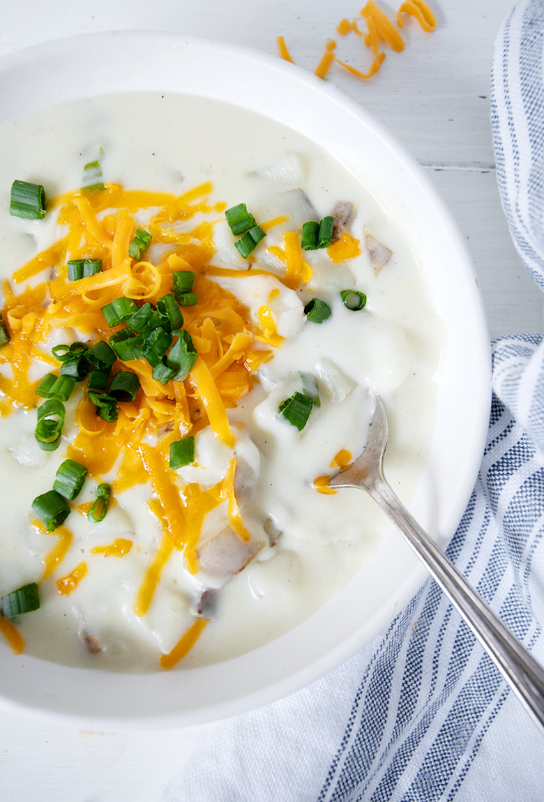 baked potato soup in white bowl, topped with cheese and green onion