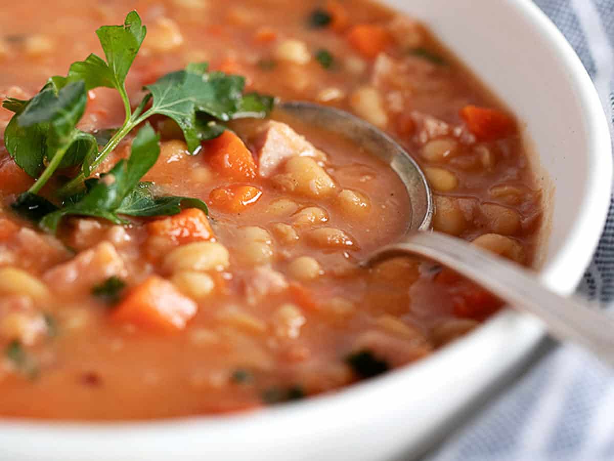 bean and ham soup in white bowl with spoon