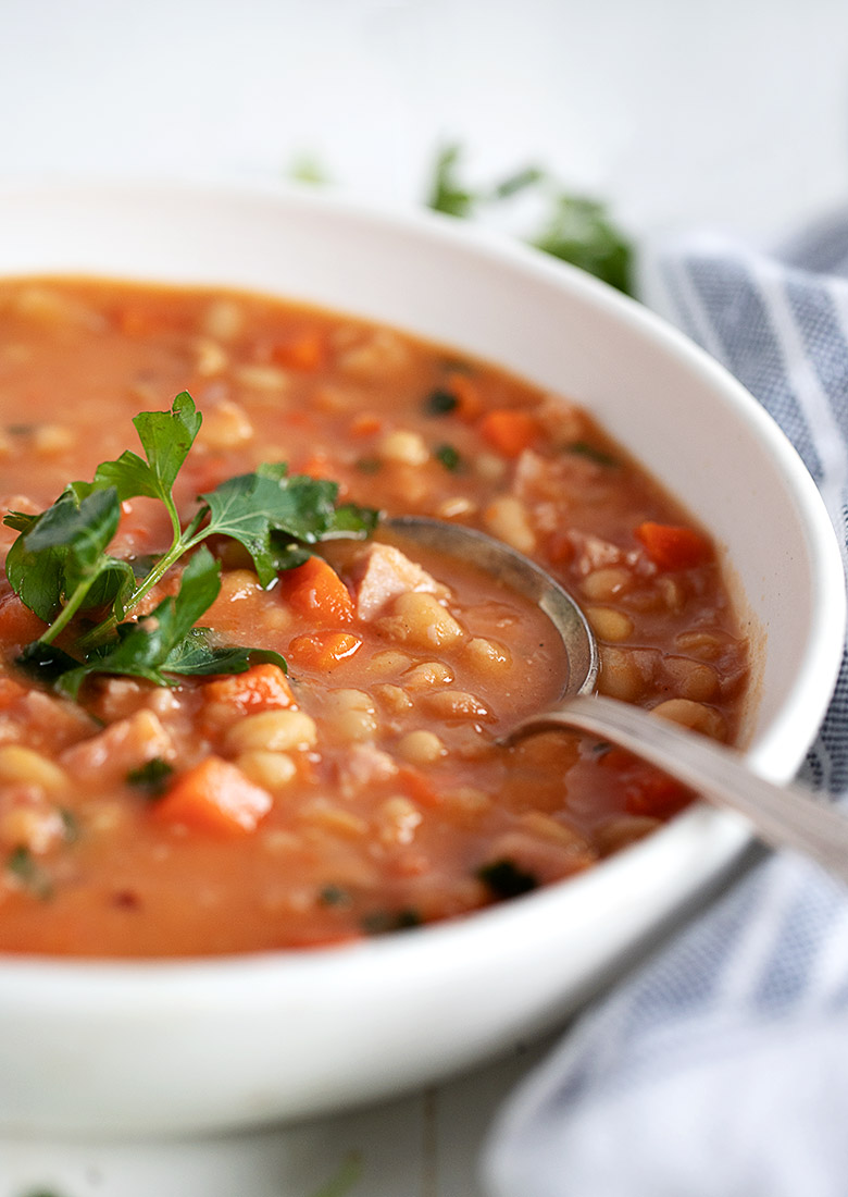 ham and navy bean soup in white bowl with spoon