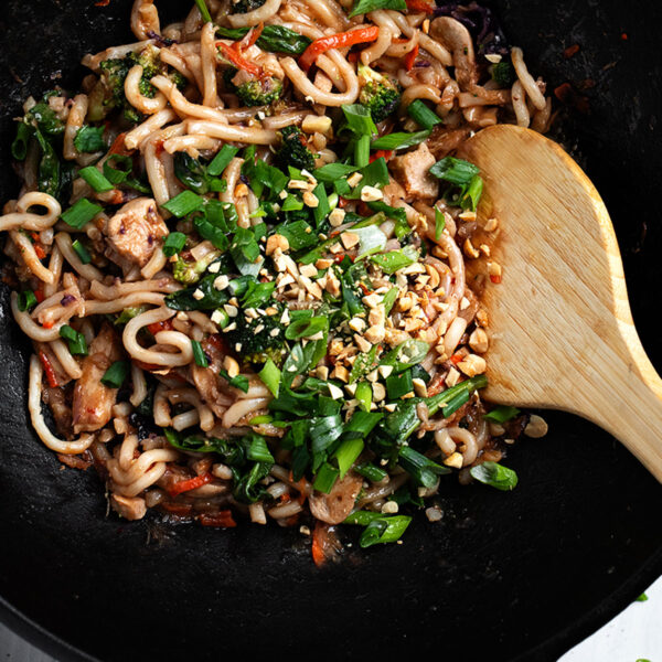 peanut noodles with chicken in wok with large spoon