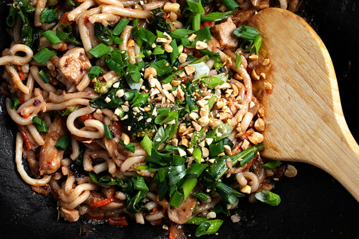 peanut noodles with chicken in wok with large spoon