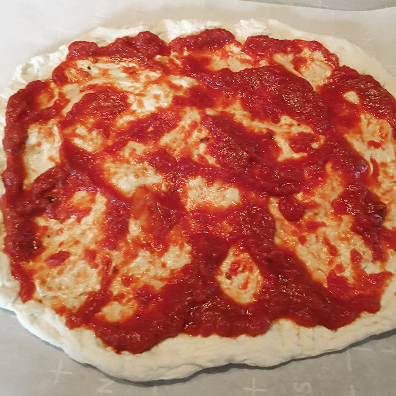 adding sauce to homemade pizza dough