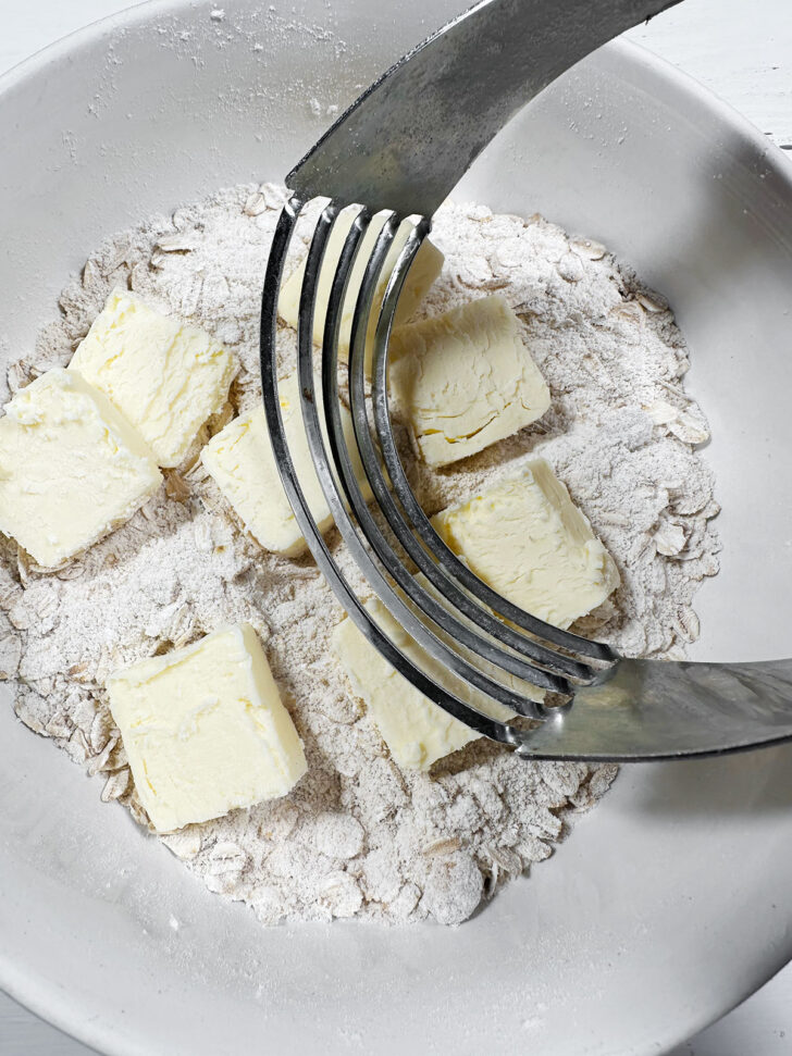 Cutting the cold butter into the flour mixture with a pastry cutter.