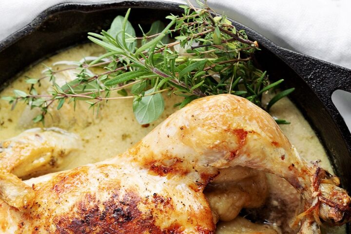 whole chicken in skillet with sauce and herbs from above