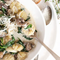 creamy gnocchi with mushrooms and spinach in white bowl