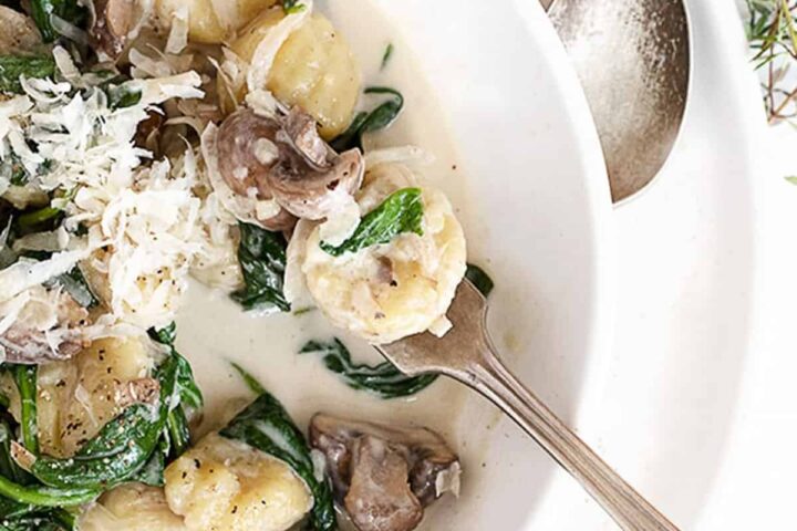 creamy gnocchi with mushrooms and spinach in white bowl