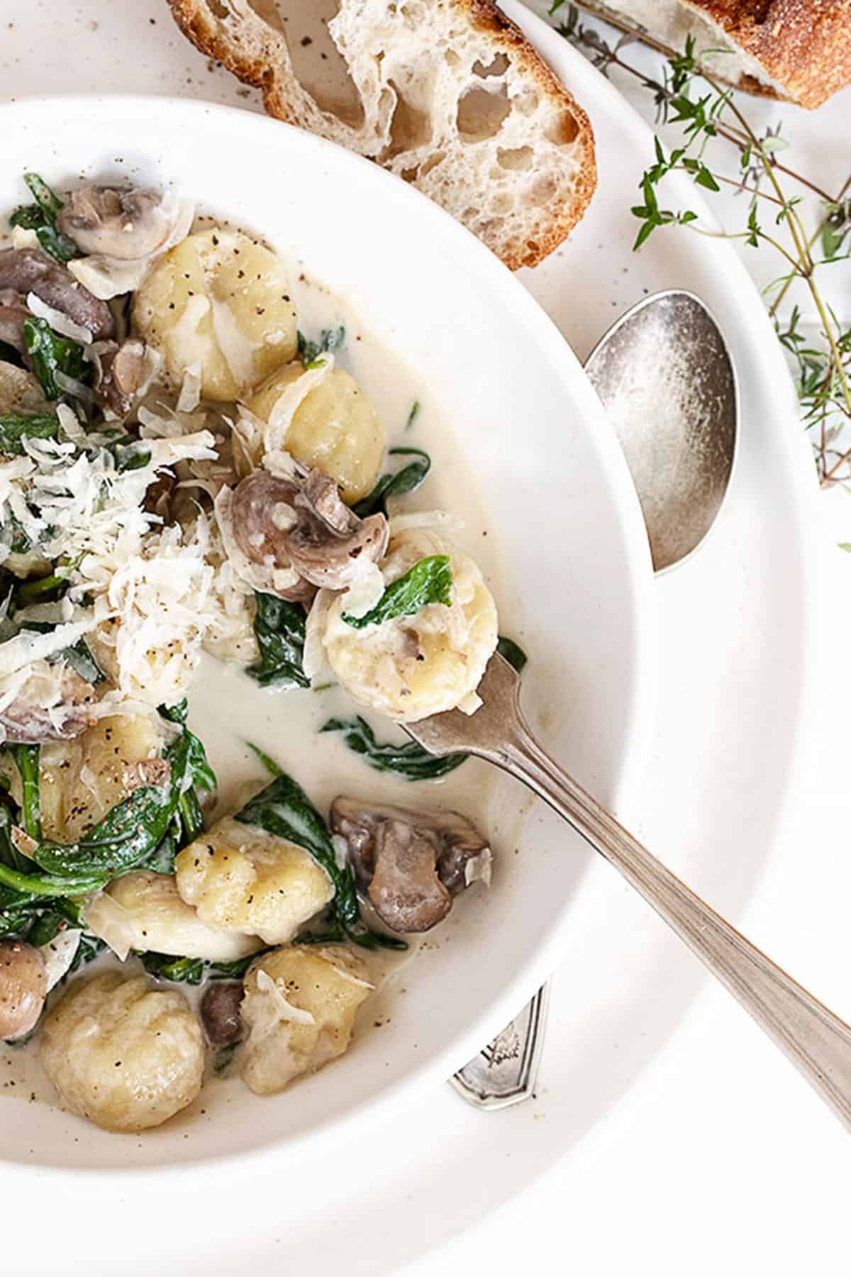 creamy gnocchi with mushrooms and spinach in white bowl