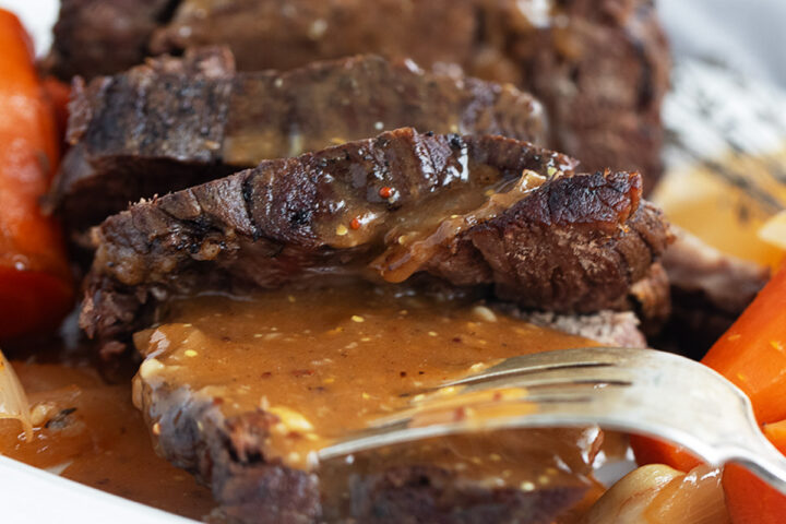 Pot roast with horseradish gravy sliced on a plate.