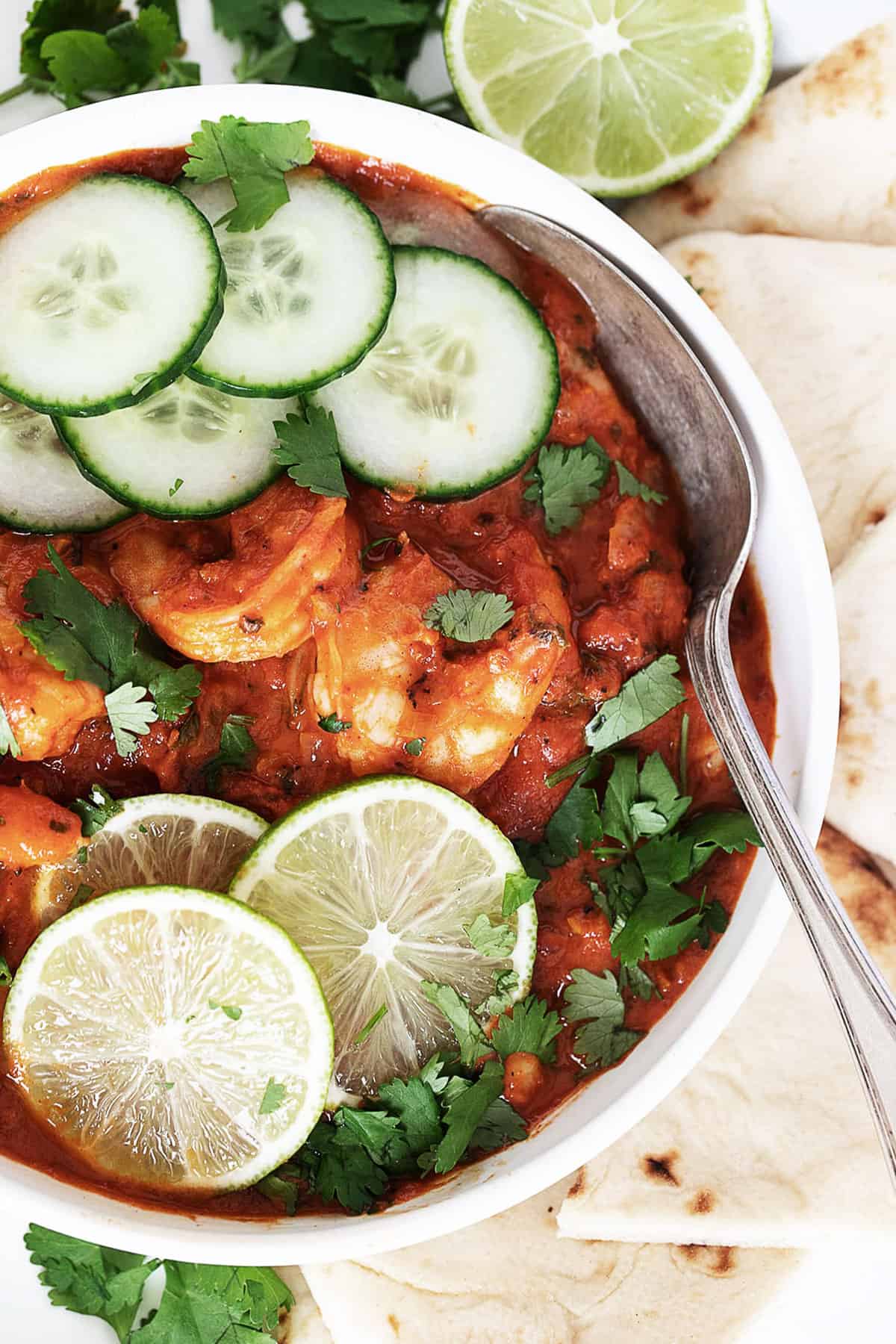 Indian butter shrimp in white bowl with lime and cucumber slices