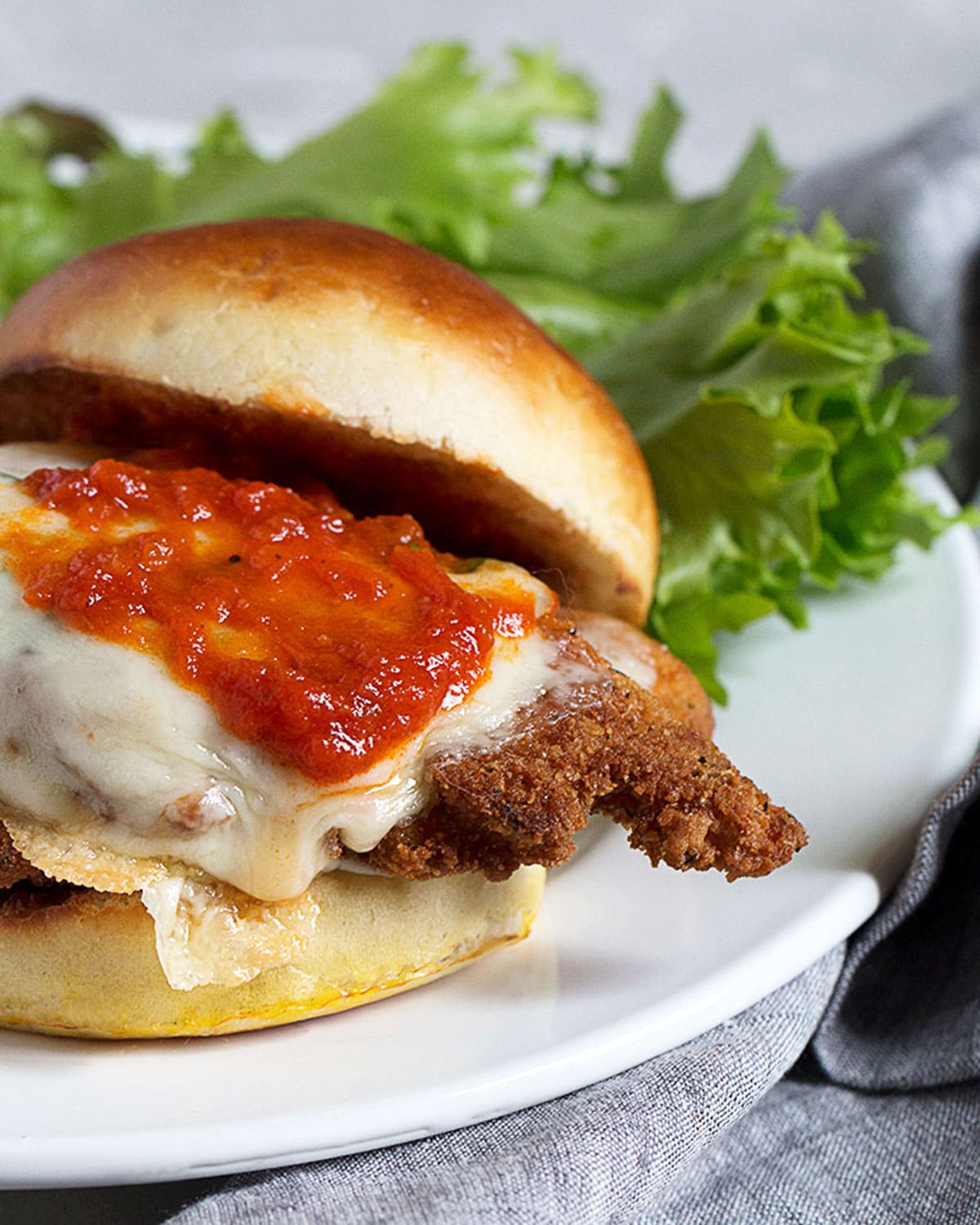 chicken parmesan on a bun on plate with lettuce