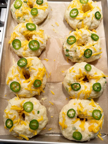 bagels topped with more cheddar cheese and jalapeno slices before baking