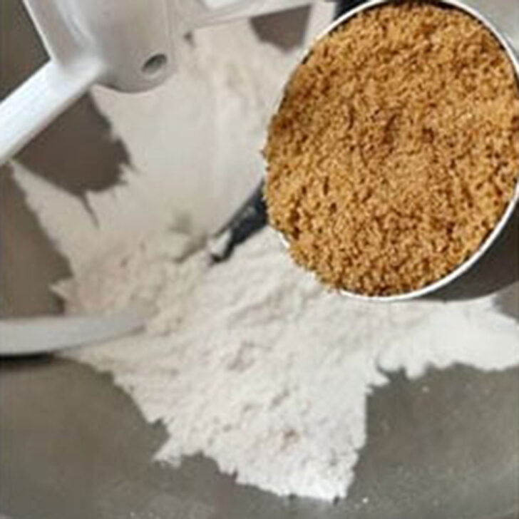Adding the brown sugar to the flour in the bowl of a mixer.