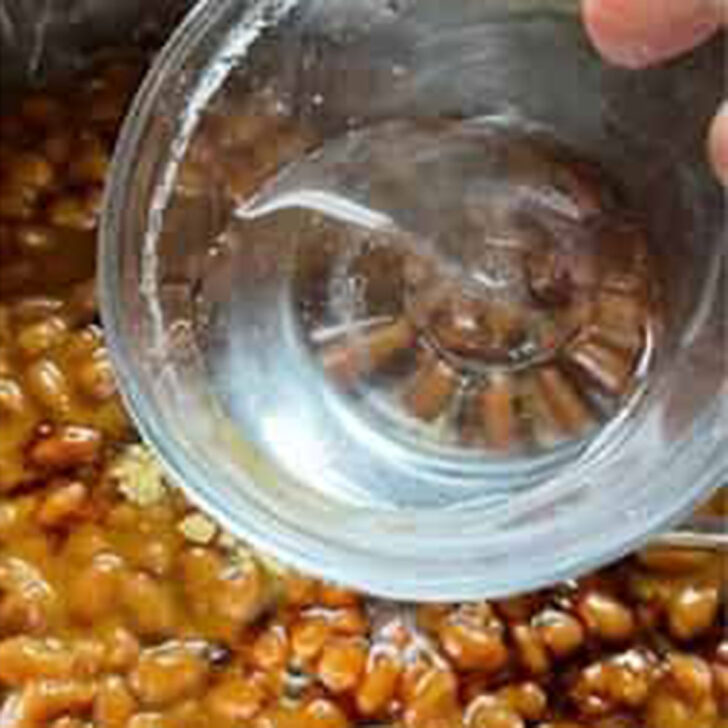 Adding vinegar to the pork and beans mixture.