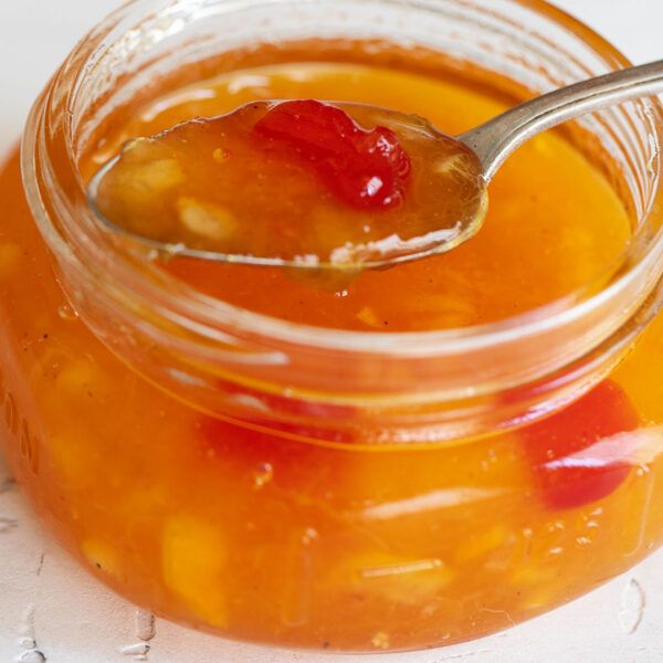 Peach orange and cherry marmalade in a small jar with a spoon.