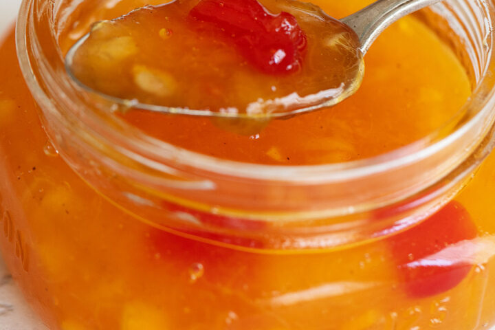Peach orange and cherry marmalade in a small jar with a spoon.