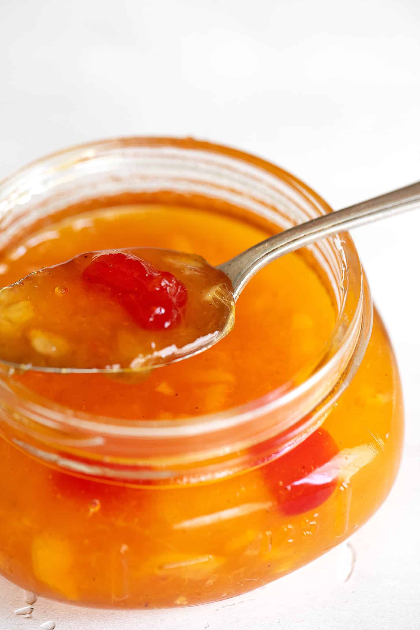 Peach orange and cherry marmalade in a small jar with a spoon.