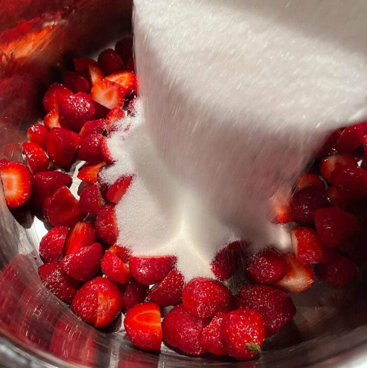Adding the white sugar to the strawberries in a cooking pot.