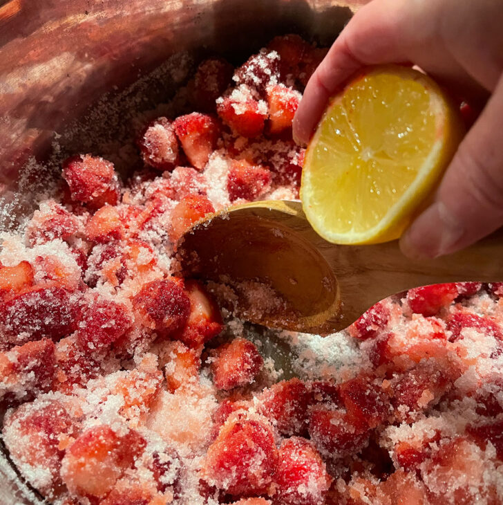 Adding lemon juice to the pot with the sugar and strawberries.