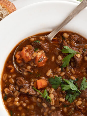 beef and barley soup in white bowl with bread on the side