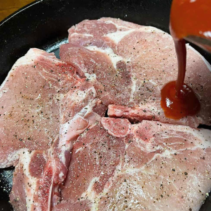 Pouring the homemade BBQ sauce over the pork chops in the skillet before baking.