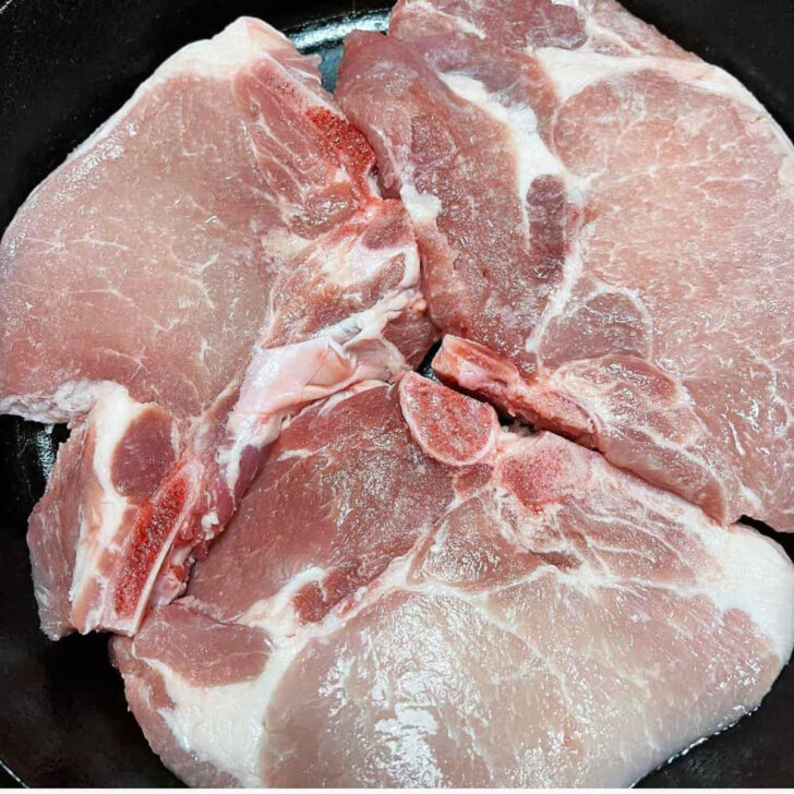 Bone-in pork chops in a cast iron skillet before cooking.