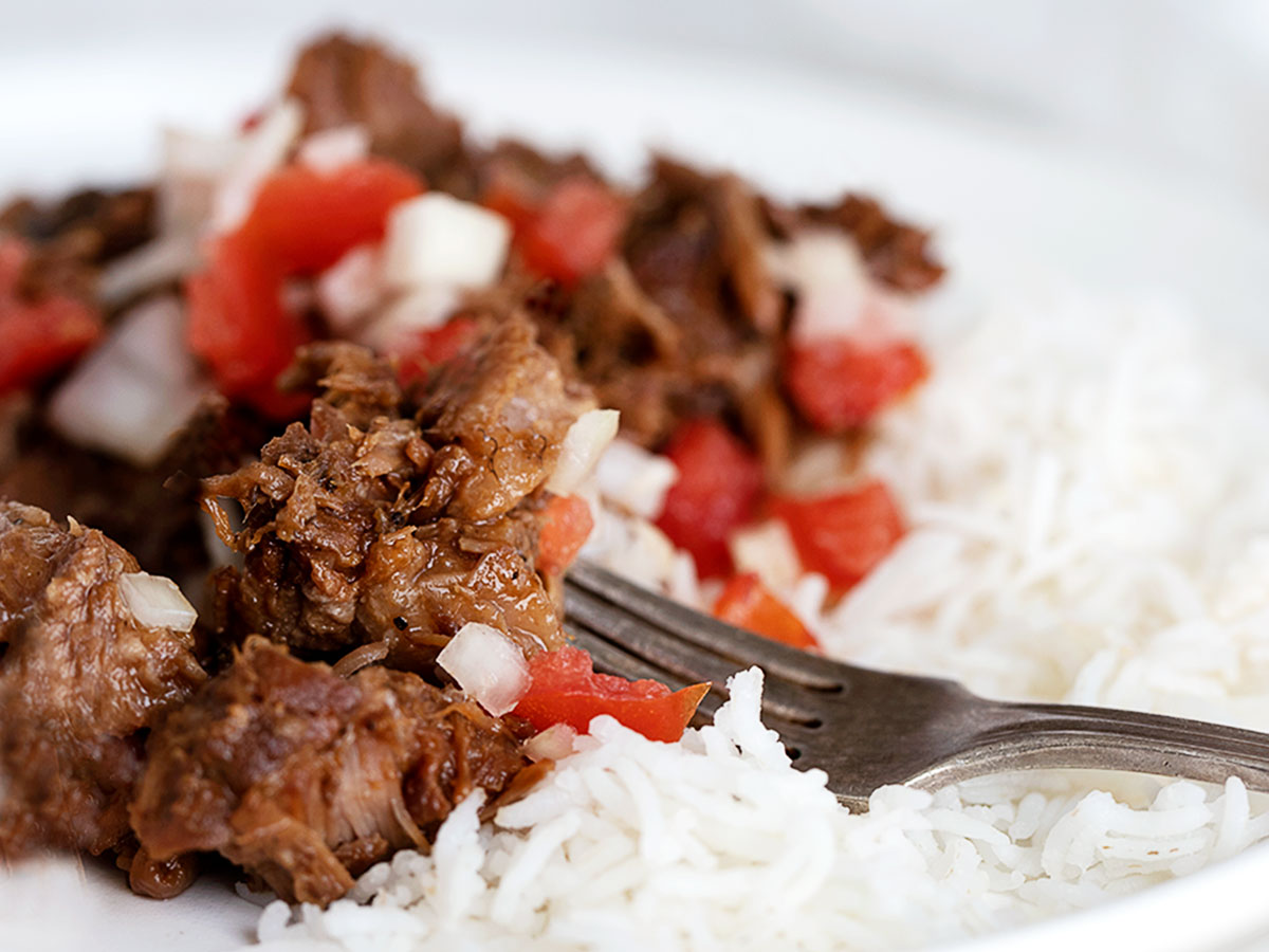 pork adobo on plate with rice and tomato onion garnish