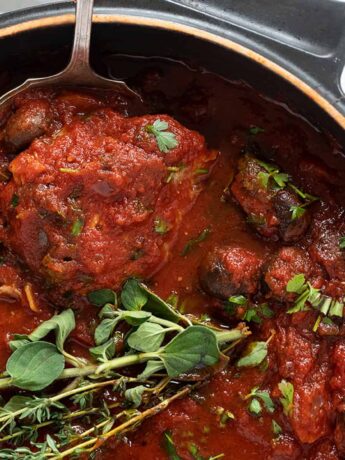 chicken cacciatore in pan with spoon and herbs