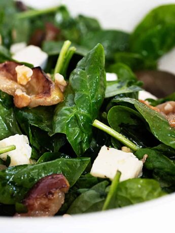 warm spinach salad in bowl with roasted apples and brie