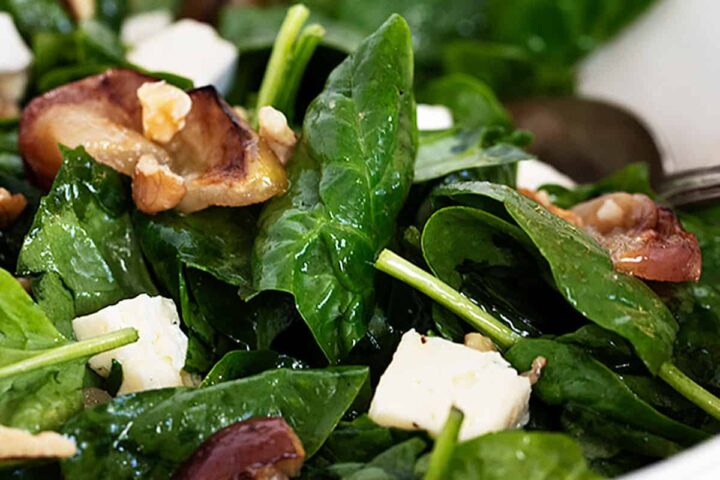 warm spinach salad in bowl with roasted apples and brie