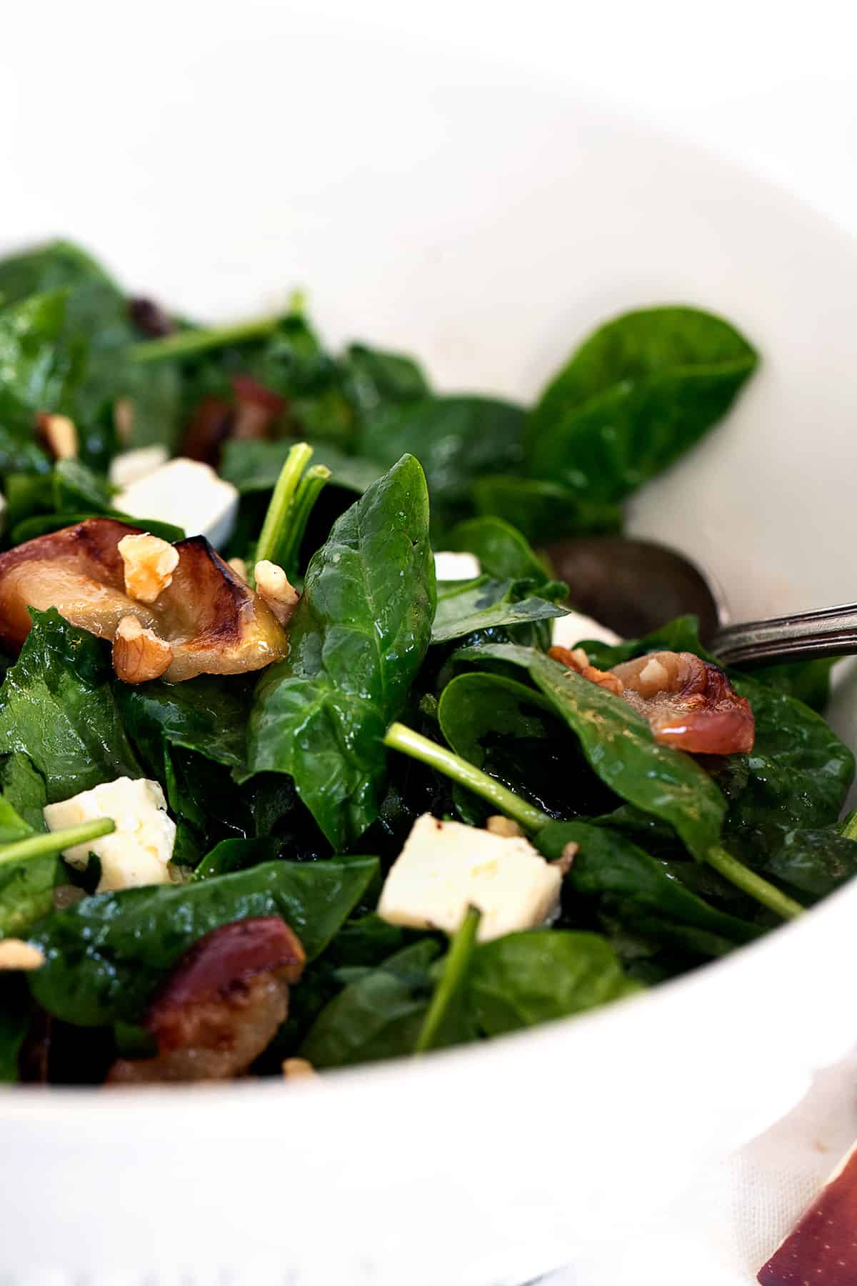 warm spinach salad in bowl with roasted apples and brie