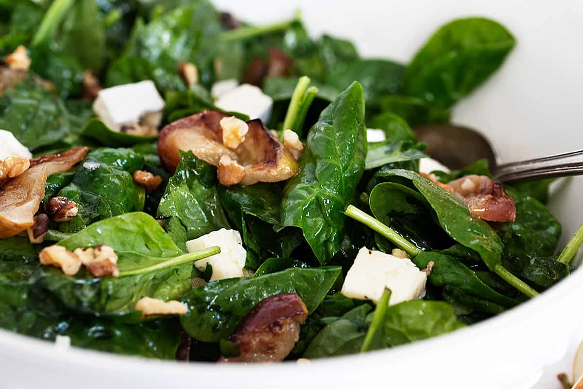 warm spinach salad in bowl with roasted apples and brie