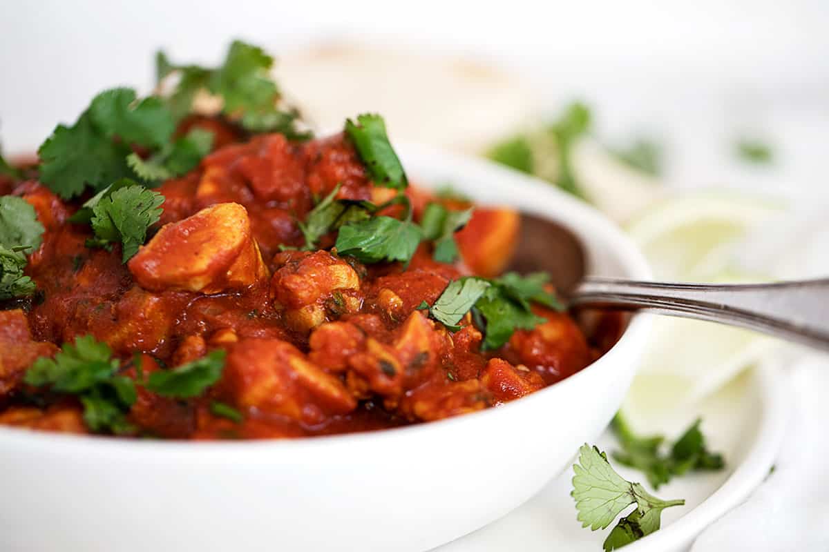 chicken madras in white bowl with lime and naan