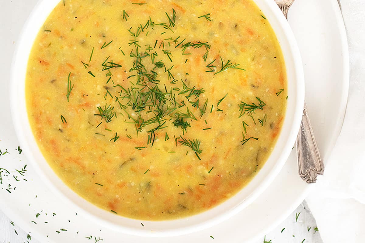 Polish potato and dill pickle soup in white bowl with spoon