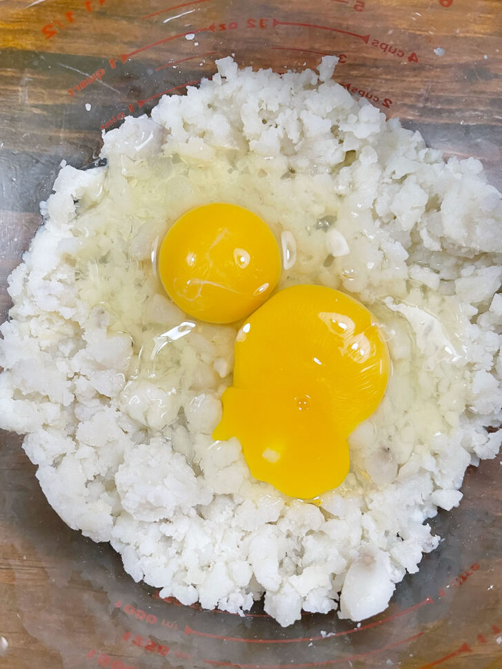 Adding eggs to mashed potatoes in bowl.