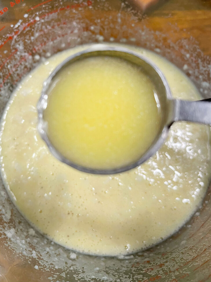 Adding melted butter to mashed potatoes in bowl.