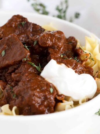 Hungarian beef paprikash in white bowl with sour cream