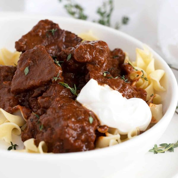 Hungarian beef paprikash in white bowl with sour cream