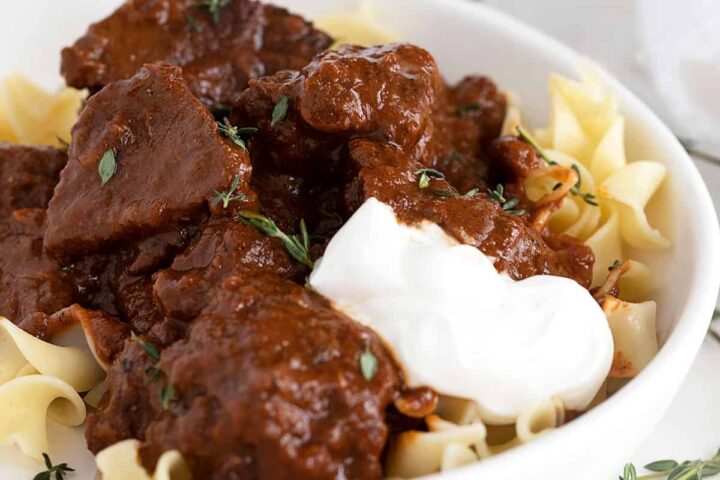 Hungarian beef paprikash in white bowl with sour cream