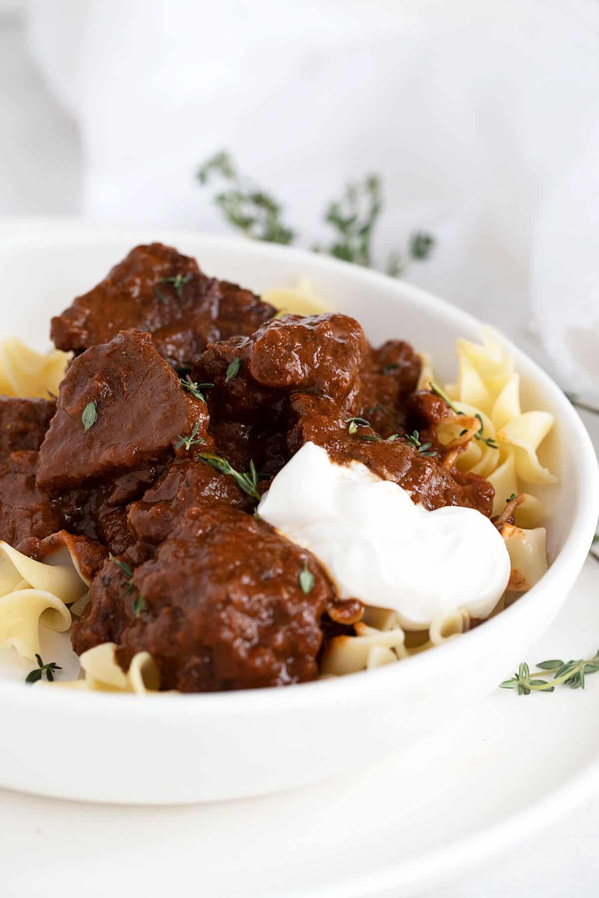 Hungarian beef paprikash in white bowl with sour cream