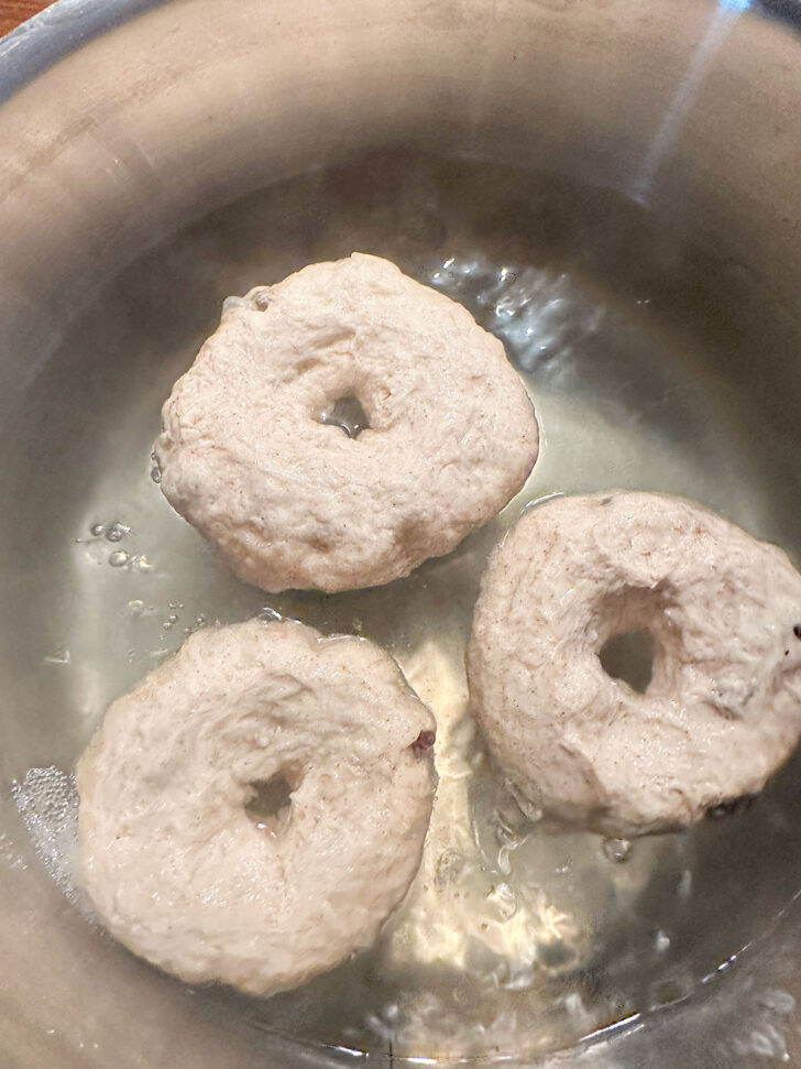 Bagels being boiled in large pot.